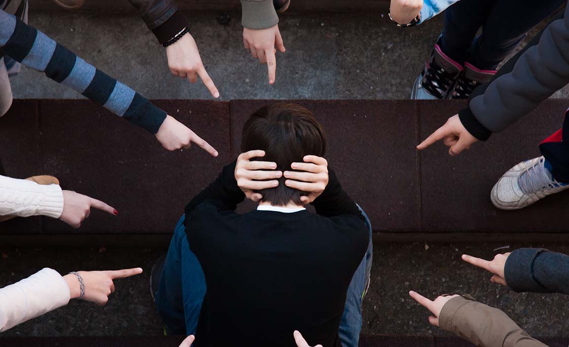 Foto de un niño con las manos en la cabeza rodeado de otros que lo señalan