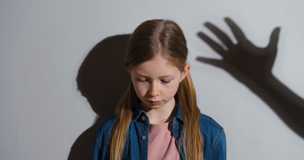niña mirando al suelo y sombra de una mano a punto de pegarle